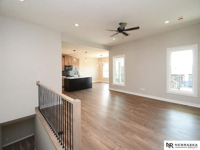 unfurnished living room with sink, wood-type flooring, and ceiling fan with notable chandelier