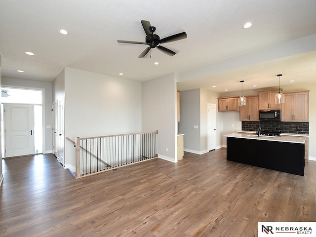 kitchen with a kitchen island with sink, dark hardwood / wood-style floors, pendant lighting, decorative backsplash, and light brown cabinetry