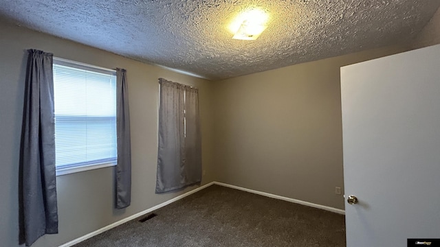 unfurnished room with a textured ceiling and dark carpet