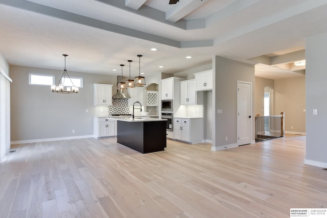 kitchen featuring appliances with stainless steel finishes, decorative light fixtures, white cabinets, light hardwood / wood-style floors, and an island with sink