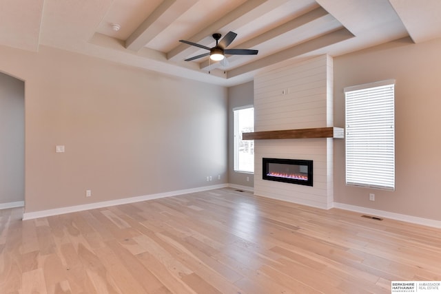 unfurnished living room with a large fireplace, ceiling fan, light hardwood / wood-style floors, and a tray ceiling