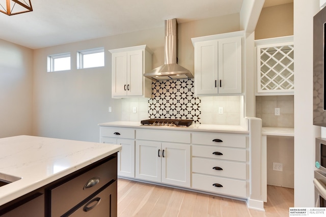 kitchen featuring stainless steel gas stovetop, wall chimney exhaust hood, white cabinets, and light hardwood / wood-style flooring