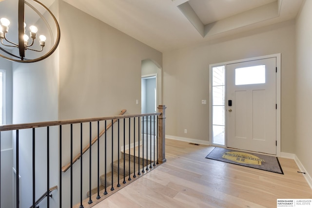 entrance foyer featuring a raised ceiling, light hardwood / wood-style flooring, and a notable chandelier