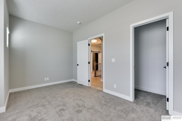 unfurnished bedroom featuring light carpet and a barn door