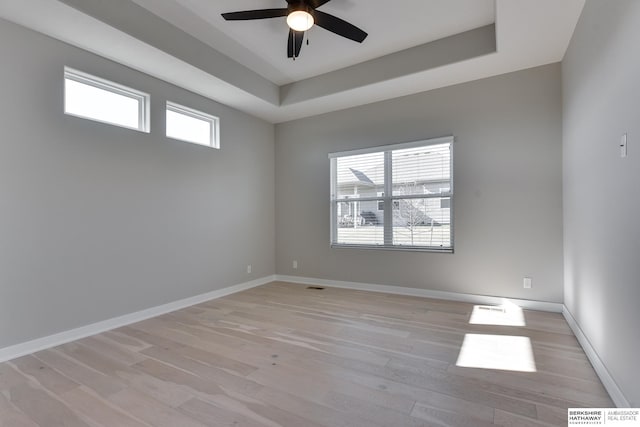 unfurnished room with a tray ceiling, ceiling fan, plenty of natural light, and light wood-type flooring