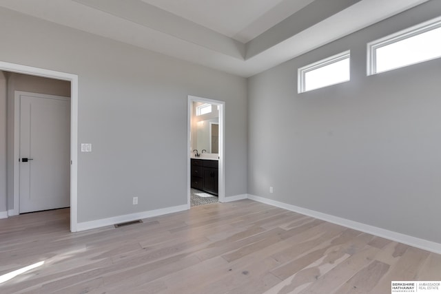 unfurnished bedroom featuring ensuite bathroom, sink, and light hardwood / wood-style flooring