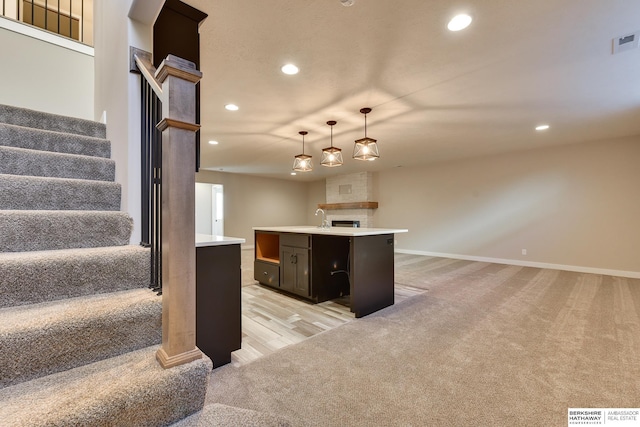 kitchen with sink, a kitchen island, decorative light fixtures, a large fireplace, and light colored carpet