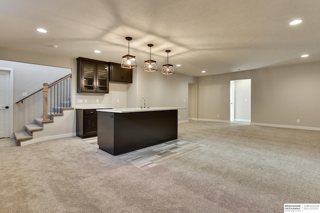 kitchen with dark brown cabinetry, a kitchen island with sink, hanging light fixtures, and light carpet