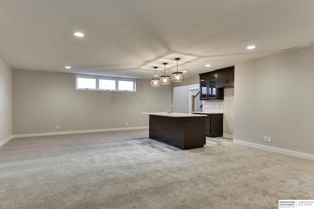 kitchen featuring a center island with sink, dark brown cabinets, light colored carpet, and hanging light fixtures