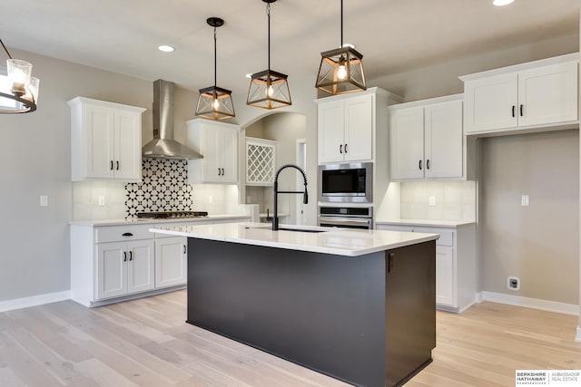 kitchen with wall chimney exhaust hood, white cabinetry, hanging light fixtures, and a kitchen island with sink