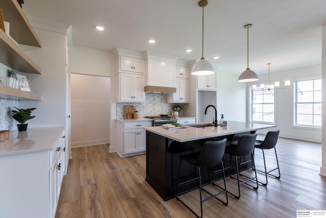 kitchen with white cabinets, light wood-type flooring, and an island with sink