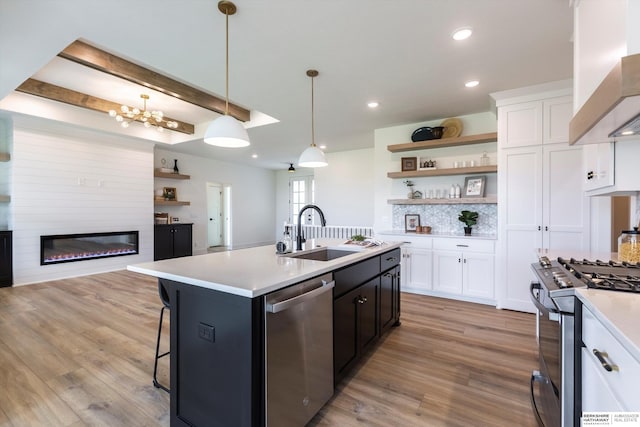 kitchen featuring wall chimney range hood, appliances with stainless steel finishes, light hardwood / wood-style flooring, and sink