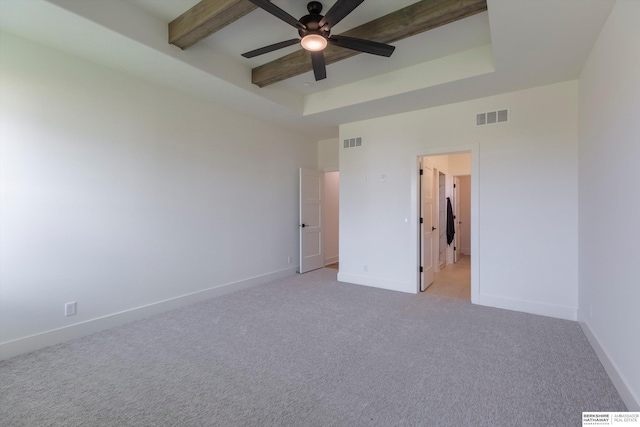 unfurnished bedroom with light carpet, ensuite bathroom, a tray ceiling, ceiling fan, and beamed ceiling