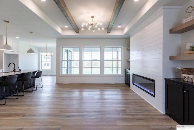 interior space featuring beam ceiling, a chandelier, light hardwood / wood-style floors, a kitchen bar, and white cabinets