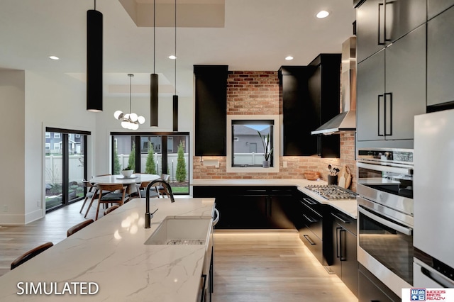 kitchen featuring appliances with stainless steel finishes, sink, light stone counters, decorative light fixtures, and wall chimney exhaust hood