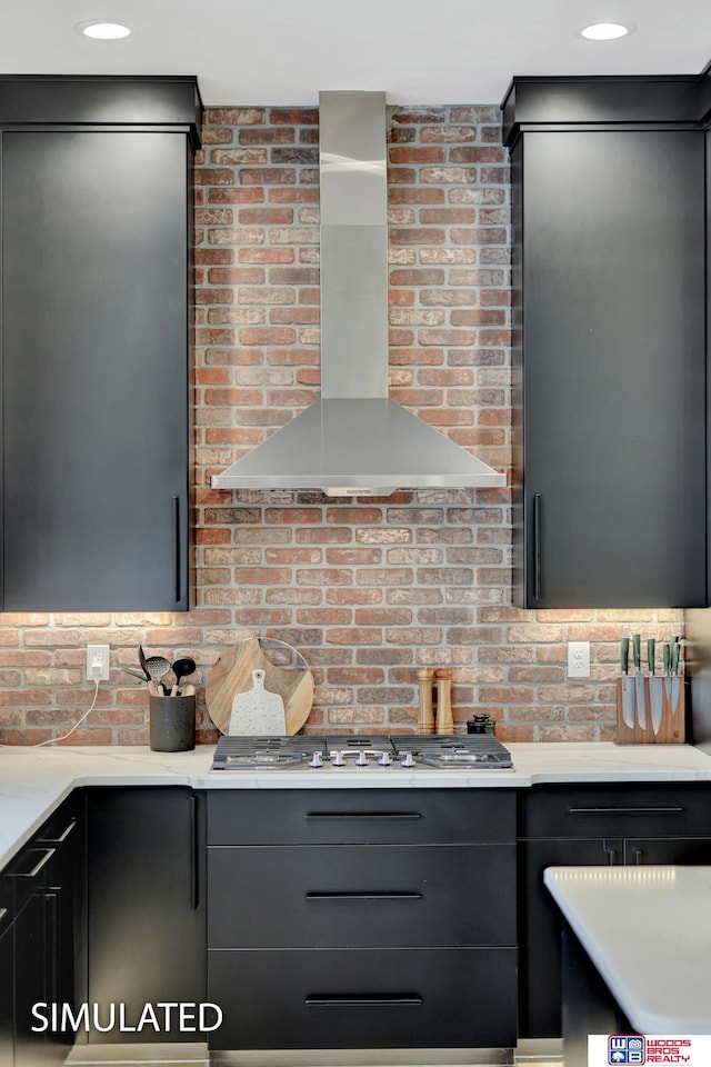 kitchen featuring stainless steel gas stovetop, brick wall, and wall chimney range hood