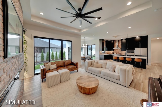 living room with a tray ceiling, light hardwood / wood-style floors, ceiling fan with notable chandelier, and a fireplace