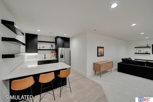 kitchen featuring light stone counters, a breakfast bar area, stainless steel fridge, and kitchen peninsula