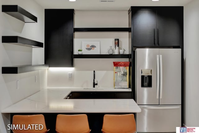 kitchen with sink, light stone counters, and stainless steel fridge with ice dispenser