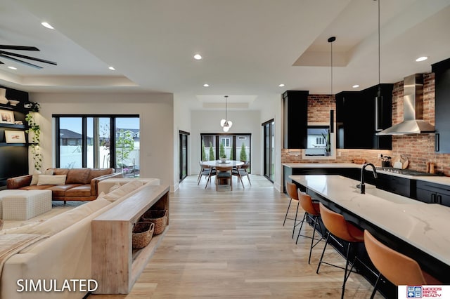 kitchen with pendant lighting, a raised ceiling, light stone countertops, and wall chimney range hood