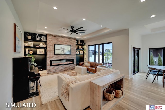 living room with a tray ceiling, light hardwood / wood-style flooring, ceiling fan, and a fireplace