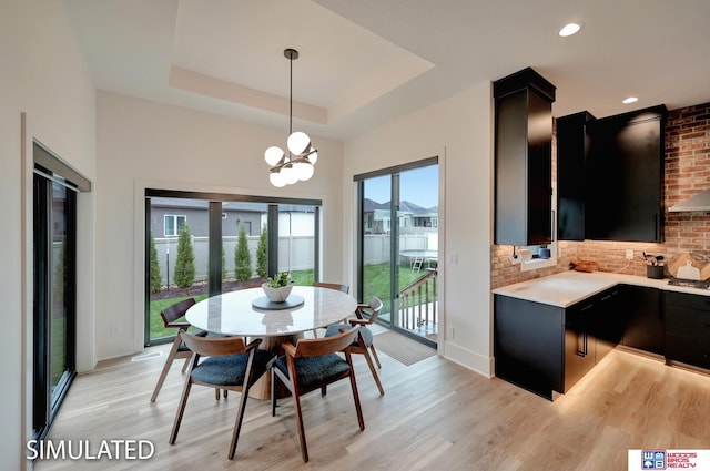 dining area featuring a tray ceiling, a notable chandelier, and light hardwood / wood-style floors