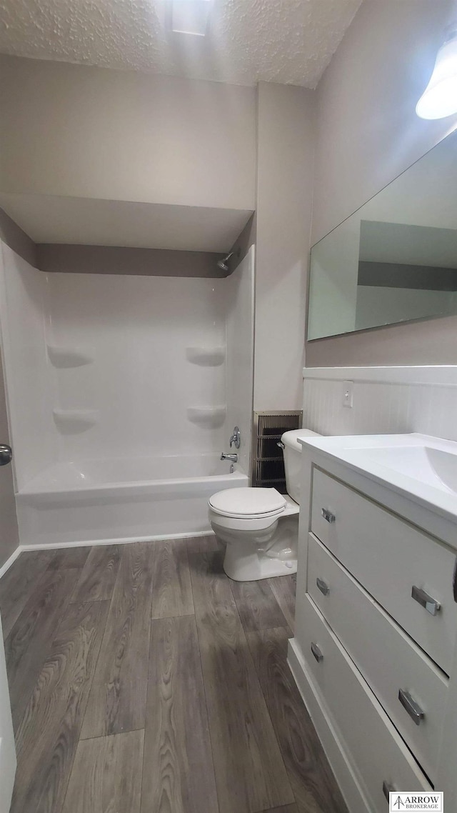 full bathroom featuring a textured ceiling, vanity,  shower combination, hardwood / wood-style flooring, and toilet