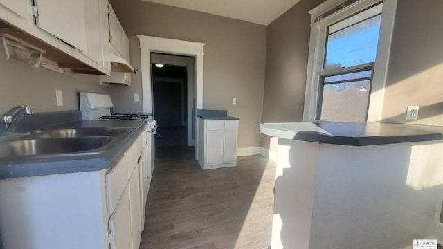 kitchen with kitchen peninsula, gas range gas stove, sink, white cabinets, and dark hardwood / wood-style floors