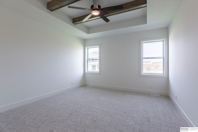 empty room with beamed ceiling, light colored carpet, ceiling fan, and a tray ceiling