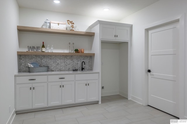 bar with backsplash, white cabinetry, and sink