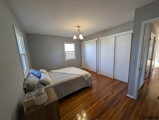 bedroom with two closets, dark wood-type flooring, and a notable chandelier