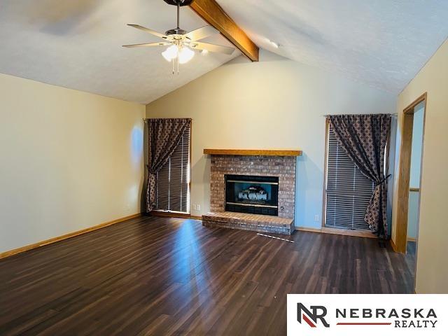 unfurnished living room with vaulted ceiling with beams, ceiling fan, a fireplace, and dark hardwood / wood-style floors