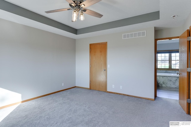 empty room with carpet flooring, a tray ceiling, and ceiling fan