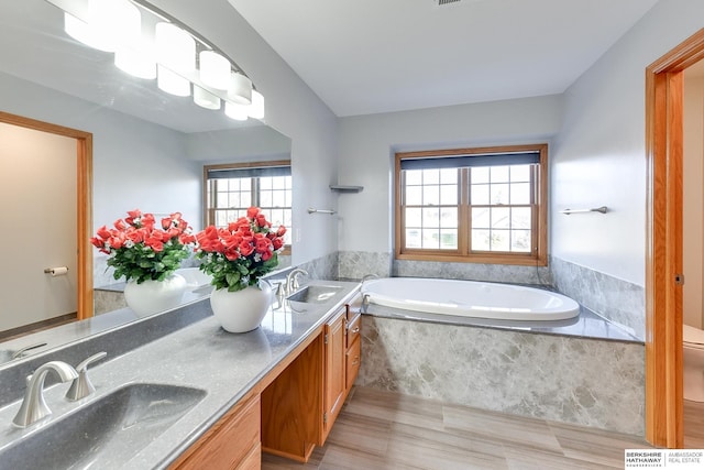 bathroom featuring vanity, a relaxing tiled tub, and toilet