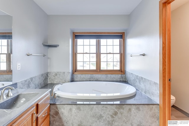 bathroom featuring tiled tub, vanity, a healthy amount of sunlight, and toilet