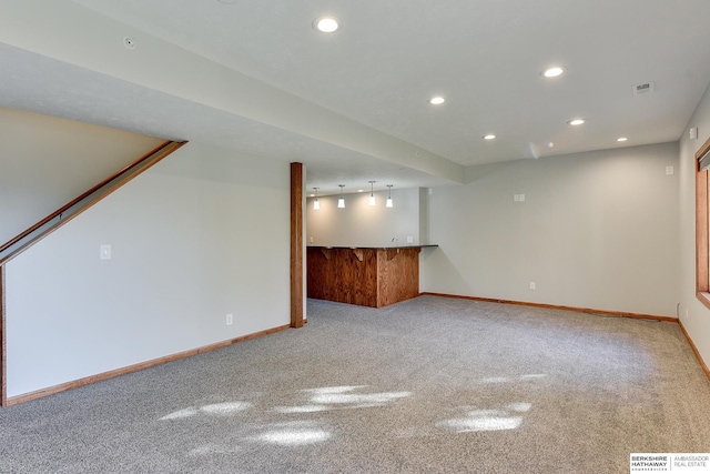 unfurnished living room featuring bar area, track lighting, and light colored carpet