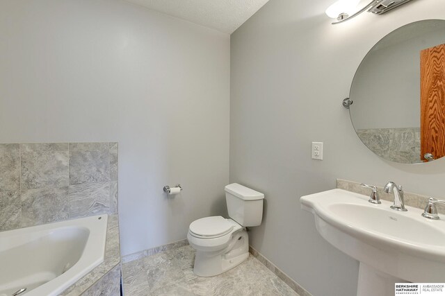 bathroom featuring sink, a textured ceiling, toilet, and tiled tub