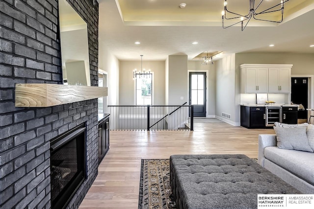 living room featuring a raised ceiling, a brick fireplace, and light wood-type flooring