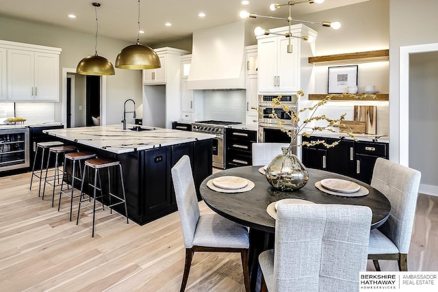 kitchen featuring hanging light fixtures, stainless steel appliances, premium range hood, a center island with sink, and white cabinets