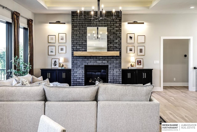 living room featuring a raised ceiling, a brick fireplace, a notable chandelier, and hardwood / wood-style flooring