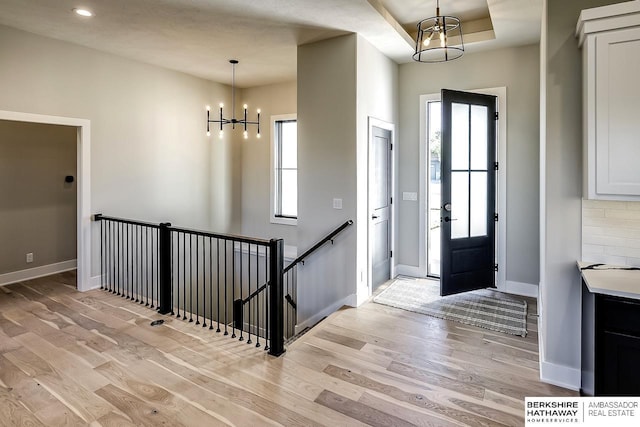 entrance foyer featuring an inviting chandelier, a raised ceiling, and light hardwood / wood-style flooring