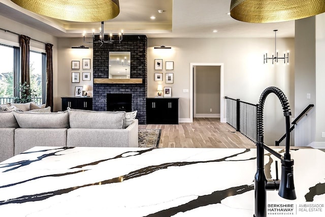 living room featuring a brick fireplace, light hardwood / wood-style floors, a tray ceiling, and an inviting chandelier