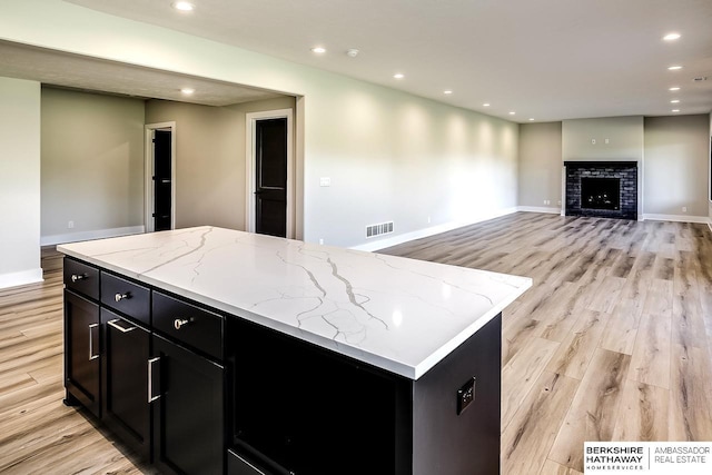 kitchen with a brick fireplace, light stone counters, a kitchen island, and light wood-type flooring