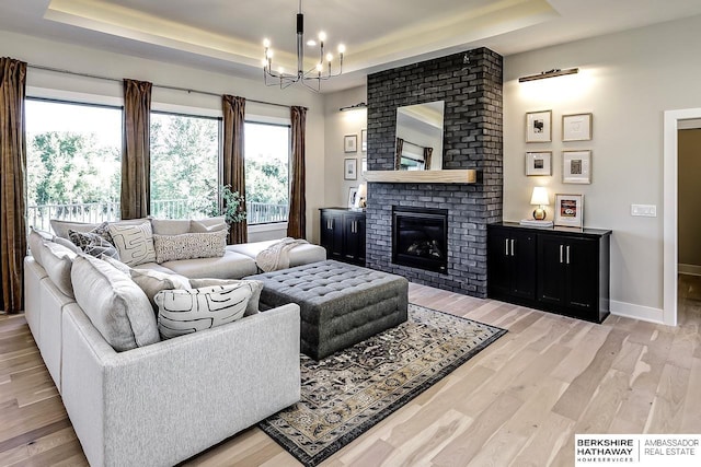 living room featuring a tray ceiling, a fireplace, a notable chandelier, and light wood-type flooring