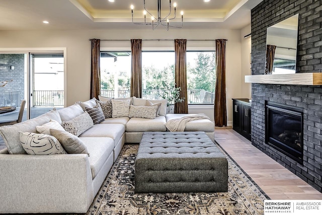 living room with a fireplace, a tray ceiling, light hardwood / wood-style flooring, and a notable chandelier