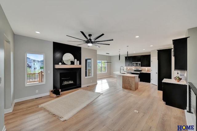 kitchen featuring a large fireplace, stainless steel appliances, sink, a center island with sink, and light hardwood / wood-style flooring