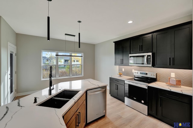 kitchen featuring light stone counters, pendant lighting, stainless steel appliances, and sink