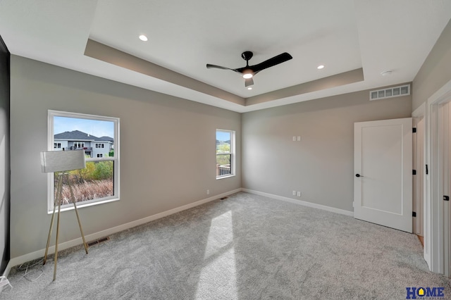 unfurnished bedroom with ceiling fan, light colored carpet, and a tray ceiling