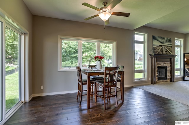 dining space featuring a stone fireplace, ceiling fan, and dark hardwood / wood-style flooring