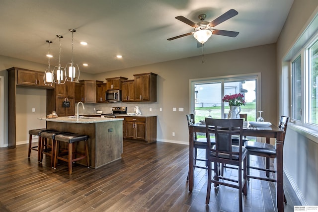 kitchen with a kitchen island with sink, light stone countertops, decorative light fixtures, dark hardwood / wood-style flooring, and stainless steel appliances